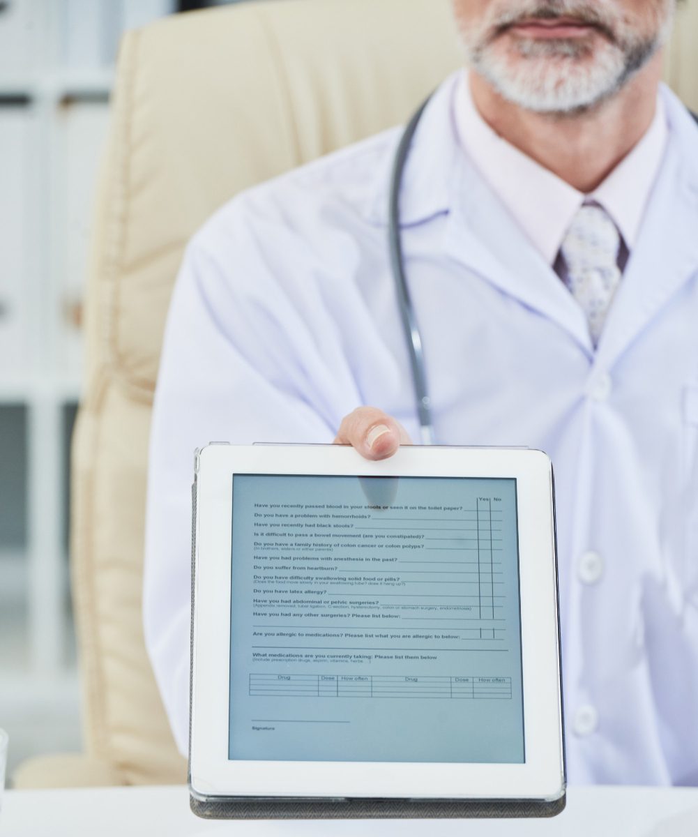 mid-section-male-doctor-seated-desk-extending-digital-questionnaire-tablet-screen-camera-img
